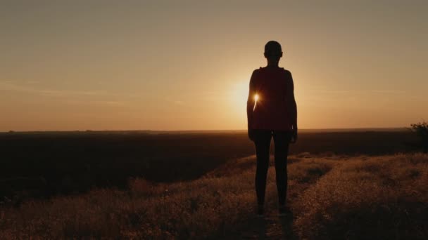 Femme mince se tient sur une colline dans les rayons du soleil couchant — Video