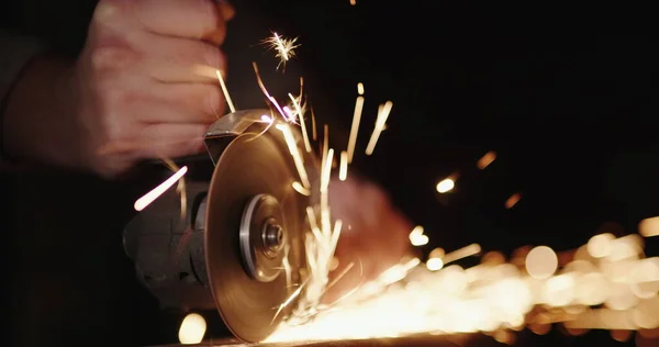 Mani di un lavoratore con un utensile elettrico, rettifica di metallo, scintille volare ai lati — Foto Stock