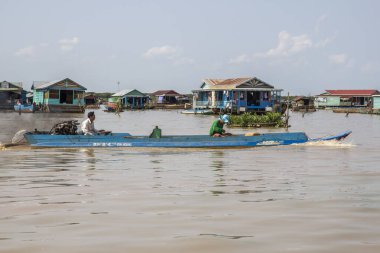 Kamboçya, Tonle Sap Gölü, Şubat 2012: Balıkçılar sudaki kulübelerin arka planına karşı bir teknede yelken açtılar. Gölde yaşayan Khmerlerin hayatı