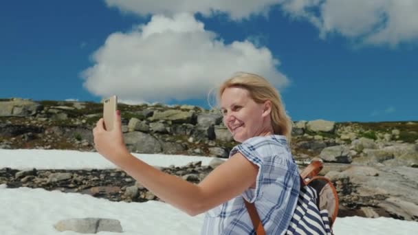 Una mujer feliz haciendo selfie en un glaciar en Noruega. Tiempo caluroso, pero la nieve no se ha derretido todavía. La increíble naturaleza de Escandinavia — Vídeo de stock