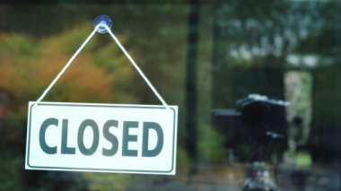 Genç bir kadın dükkanın kapısında açık bir tabela çalar..