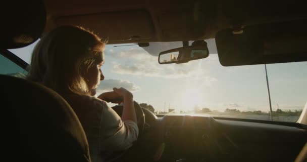 Conductora de mediana edad conduce coche, puesta de sol brilla en el parabrisas — Vídeos de Stock