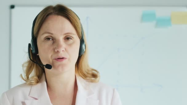 Obchodní trenér ve sluchátkách říká na pozadí desky s plány a diagramy — Stock video