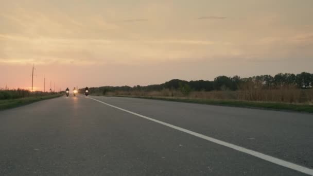 三个骑摩托车的人在日落时沿着公路开车，开车经过摄像头。慢动作视频 — 图库视频影像