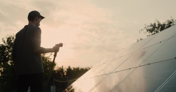 Egy férfi sziluettje, aki napelemes erőművet mos. — Stock videók