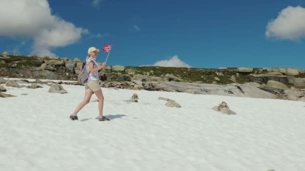 Uma mulher caminha na neve com a bandeira da Noruega. Julho Dia de Verão — Vídeo de Stock