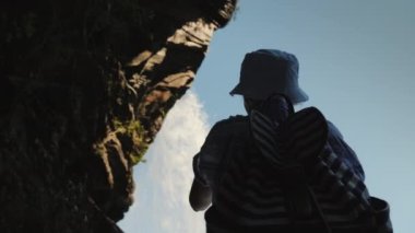 Steinsdalsfossen şelalesinin altında duran kadının düşük açılı görüntüsü bir fotoğraf çeker, üzerinde bir kaya asılı durur ve bir su akıntısı akar..