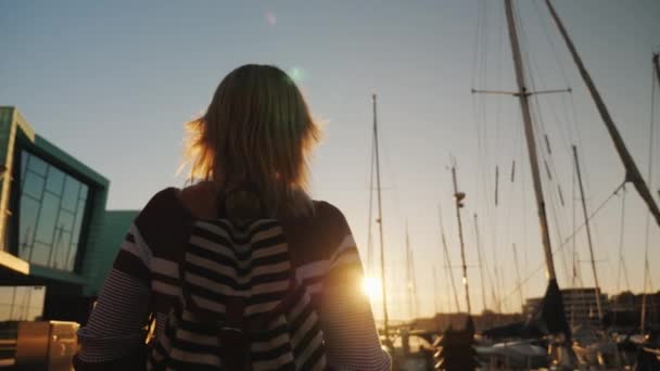 Вид сзади Молодая женщина прогуливается по престижному району Бергена рядом с пирсом с яхтами. — стоковое видео