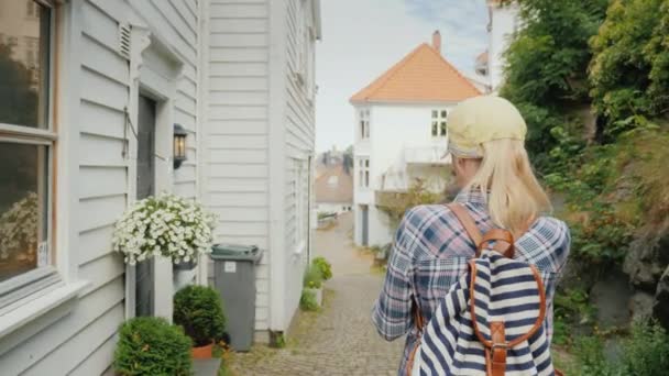 Pohled zezadu Žena kráčí úzkou uličkou starého města, používá GPS navigátor na smartphonu. Město Bergen v Norsku — Stock video