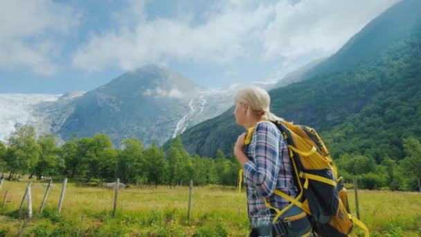 Podróżując po pięknych miejscach Skandynawii, kobieta z plecakiem spaceruje malowniczą doliną w tle gór — Wideo stockowe