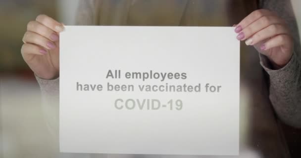 Ein Mitarbeiter hängt eine Durchsage an die Tür des Betriebs, dass alle Mitarbeiter geimpft sind und sicher zu Besuch sind — Stockvideo