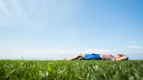 Ευτυχισμένη ξυπόλητη γυναίκα βρίσκεται στο πράσινο γρασίδι, χαίρεται τη ζέστη και το καλοκαίρι — Φωτογραφία Αρχείου