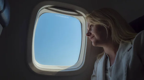 Mujer joven viajando en un avión, mirando al cielo a través del ojo de buey —  Fotos de Stock