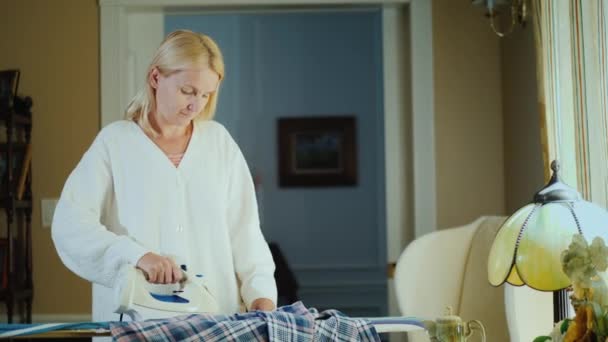 Mulher de meia idade engomar roupas em uma tábua de engomar — Vídeo de Stock