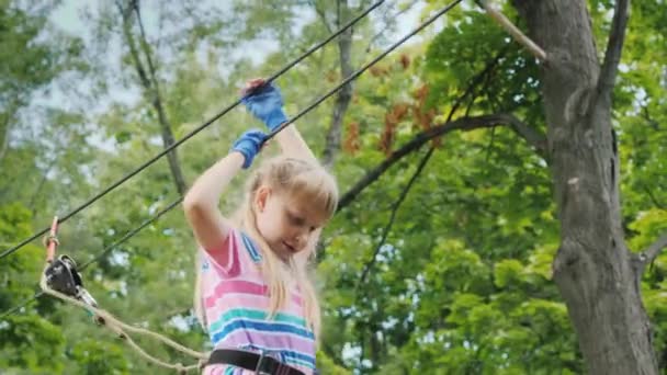 El niño se mueve sobre cuerdas altas en la copa de un árbol. Entretenimiento en campamento de verano — Vídeo de stock