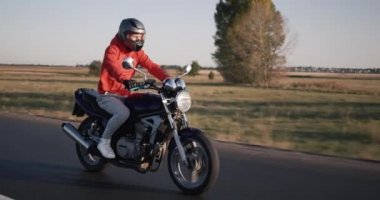 Motosikletli genç bir adam açık bir sonbahar gününde pitoresk tarlalarda gezer.