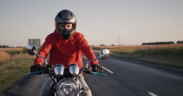 Portret van een jonge motorrijder die op een herfstdag op een motorfiets langs maïsvelden rijdt — Stockvideo
