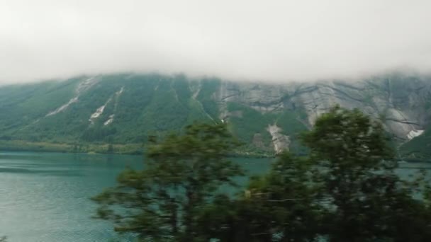 De oever van de fjord, de top van de bergen verdrinken in de wolken. Uitzicht vanuit het raam van het Noorse landschap. — Stockvideo