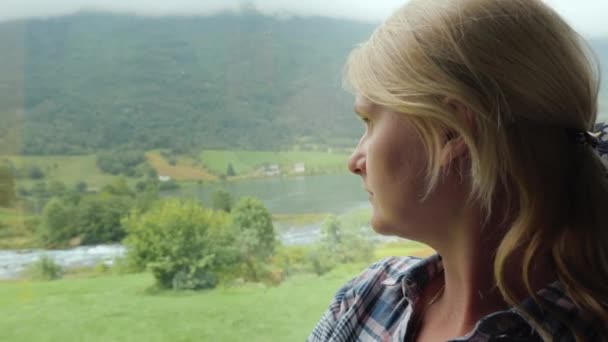 Uma mulher olha pela janela de um ônibus para a natureza da Noruega — Vídeo de Stock