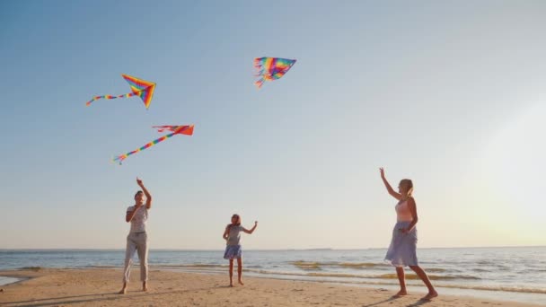 Joven familia se divierten en la playa, jugando juntos con cometas — Vídeos de Stock