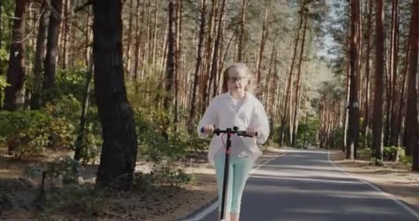 Bionda bambino sta cavalcando uno scooter nel parco — Video Stock