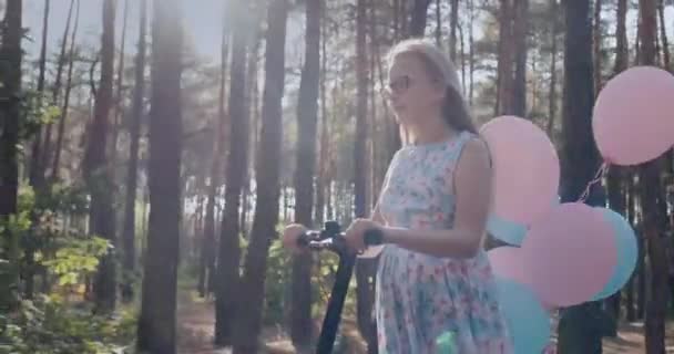 Un niño en un scooter decorado con globos pasea por el parque — Vídeo de stock