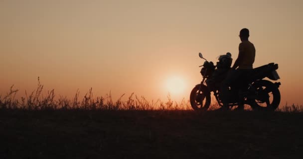 Steadicam shot: Il motociclista si è fermato ad ammirare il bellissimo tramonto. Seduto su una moto — Video Stock