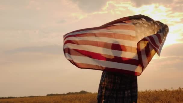 Wesoła kobieta biegnie przez pole pszenicy z flagą USA — Wideo stockowe