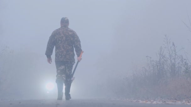 斧を手にした積極的な男が車に向かって霧の中に入る — ストック動画