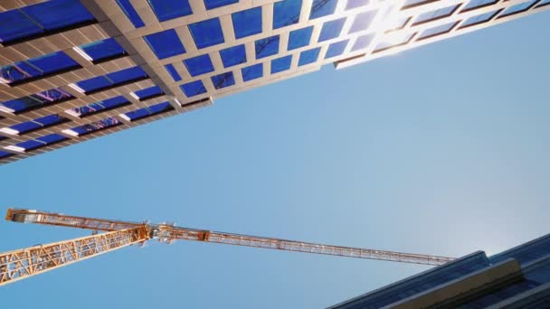 Construcción de modernos edificios de oficinas con fachadas de cristal. Vista inferior de una grúa torre grande — Vídeo de stock