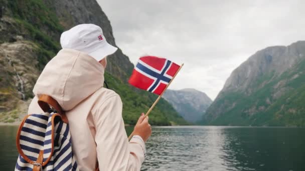 Egy norvég zászlós nő áll a tengerjáró hajó fedélzetén. Norvég fjord hajóút — Stock videók