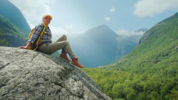 Una joven se sienta en una gran roca rodeada de altas montañas. Sola en medio de una naturaleza increíblemente hermosa — Vídeos de Stock