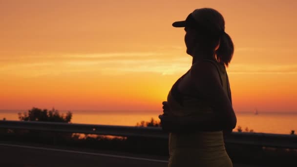 Sportliche junge Frau joggt in der Nähe des Meeres, wo die Sonne untergeht. Gesunder Lebensstil — Stockvideo