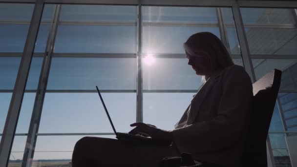 Silueta mladé podnikatelky čekající na svůj let v hale letiště, za použití notebooku — Stock video