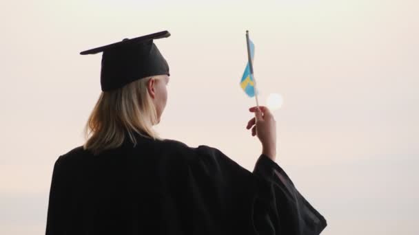 Educação na Europa - graduado em manto e boné com a bandeira da Suécia na mão — Vídeo de Stock