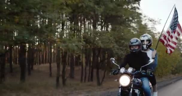 Un par de motociclistas viajan en motocicleta, seguidos de una bandera estadounidense. Concepto del Día de la Independencia — Vídeos de Stock