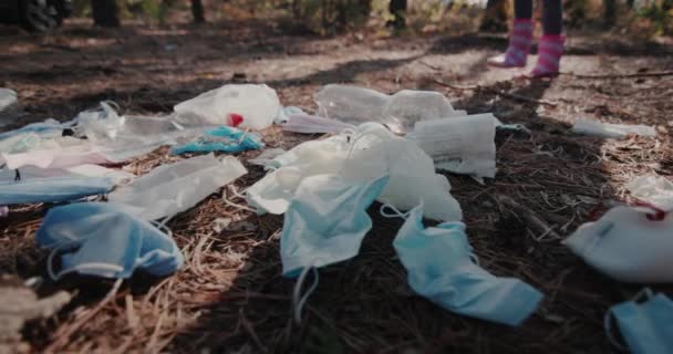 I piedi di bambini in stivali - cammina attraverso i boschi oltre una pila di immondizia fatta di maschere mediche. Concetto di questioni ambientali — Video Stock