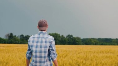 Çiftçinin arkasından bir manzara, elini buğday tarlasının üzerine kaldırıyor hoş bir jest olarak.
