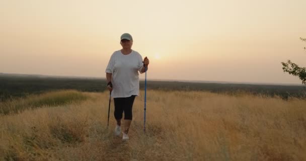 Μια ηλικιωμένη γυναίκα με σκανδιναβικά μπαστούνια περπατά μπροστά μέσα από ένα γραφικό σημείο — Αρχείο Βίντεο