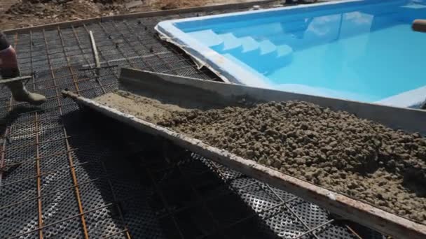 Beton fließt die Dachrinnen hinunter, wo Arbeiter Pflastersteine rund um den Pool anlegen. — Stockvideo