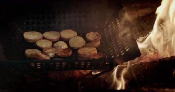 Шматочки картоплі смажать на сковороді на грилі, поруч із полум'ям сковороди та гарячим вугіллям — стокове відео
