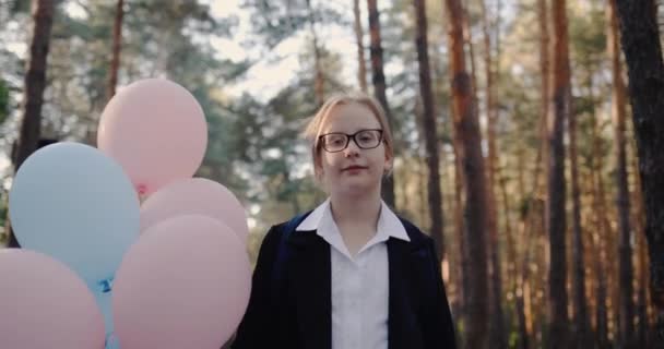 Portret uczennicy z balonami, stoi w parku z wysokimi sosnami — Wideo stockowe