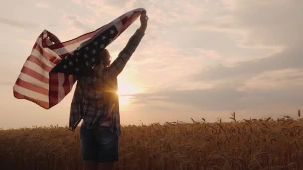 Amerikan bayrağı taşıyan bir kadın buğday tarlasında güneşte koşuyor. — Stok video