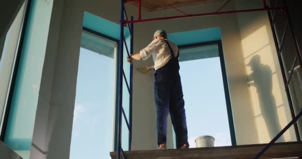 Художник призначає стіну, височіє на риштуванні всередині будинку — стокове відео