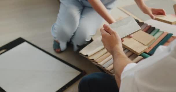 Deux conjoints choisissent une finition pour leur maison, regardez des échantillons de bois, de tissu et de papier peint. — Video