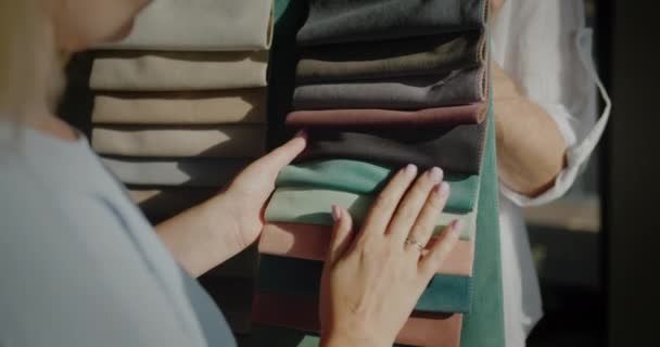 O comprador escolhe o tecido na loja têxtil, o vendedor detém amostras com tecido multicolorido — Vídeo de Stock