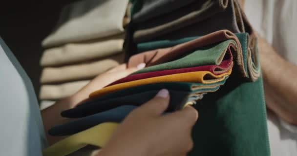 Покупатель выбирает ткань в текстильном магазине, продавец держит образцы с разноцветной тканью — стоковое видео