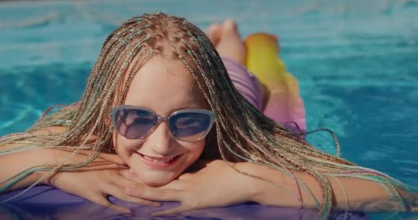 Retrato de una chica con coletas afro, nada sobre un colchón inflable en la piscina, descansando y disfrutando del resto — Vídeo de stock