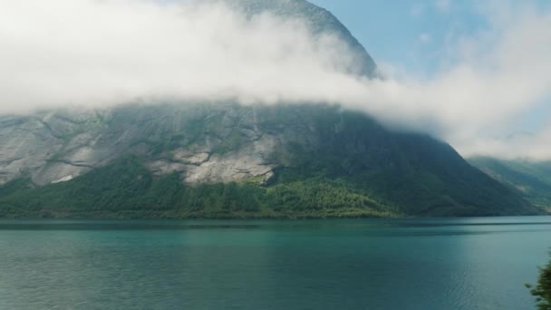 De oever van de fjord, de top van de bergen verdrinken in de wolken. Uitzicht vanuit het raam van het Noorse landschap. — Stockvideo