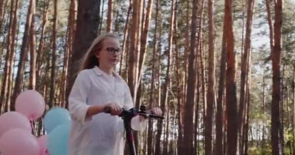 Parkta elektrikli scooter kullanan bir kız, mobiletin arkası balonlarla görülebilir. — Stok video